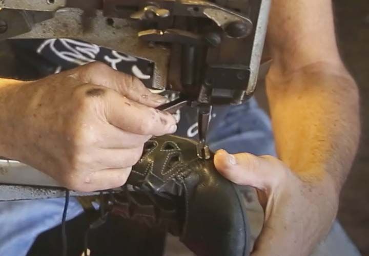 a mans hands stitching a pair of shoes using an large industrial sewing machine