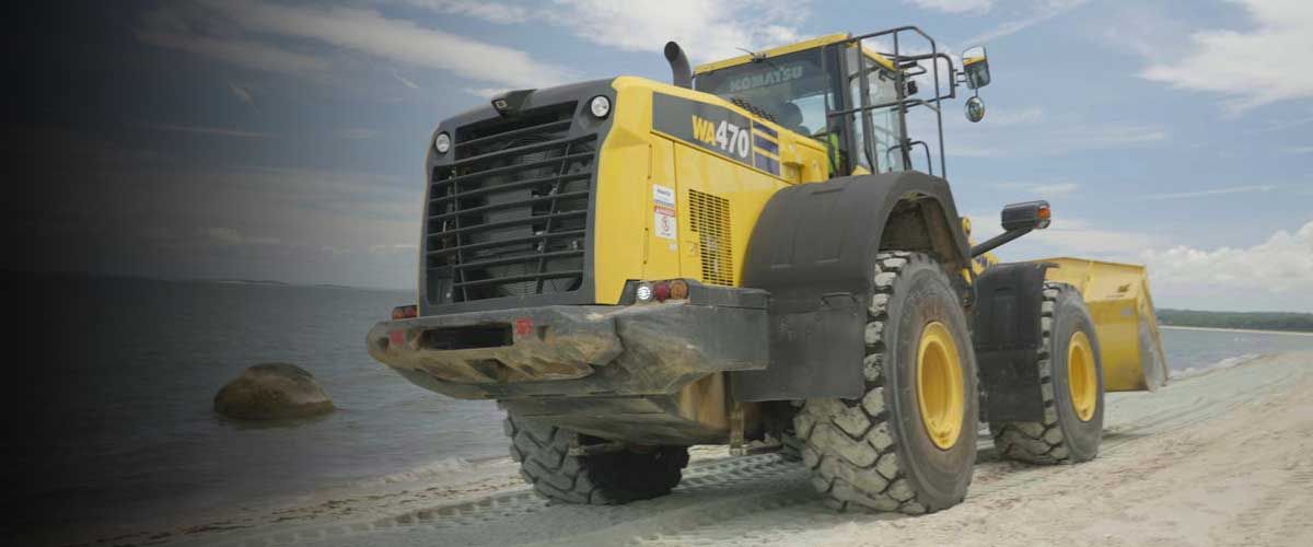 a large yellow backhoe driving along the beach